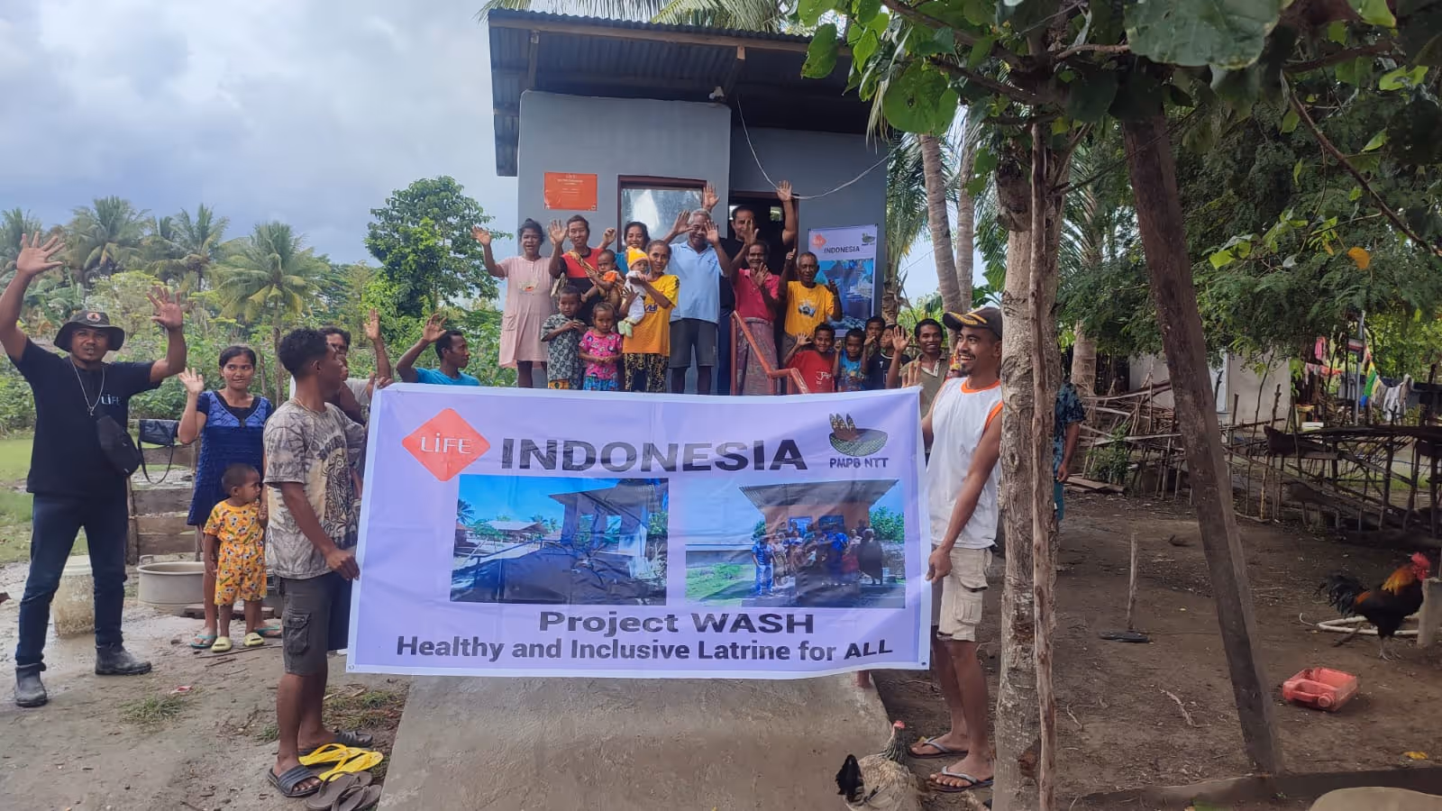 Habitants rassemblés derrière une banderole LIFE Indonesia « Project WASH », devant une latrine neuve, en agitant la main