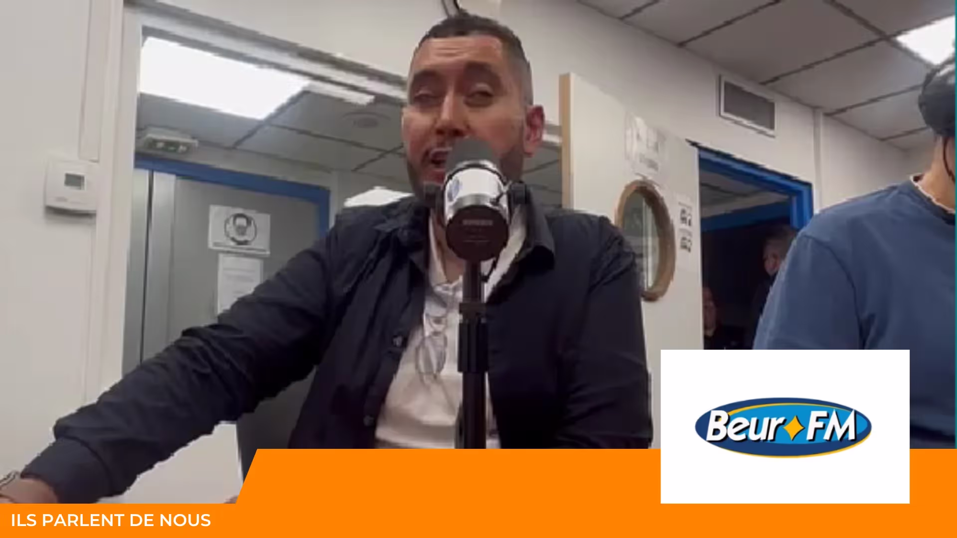 Homme parlant devant un micro dans un studio de radio, logo Beur FM et bandeau « Ils parlent de nous »