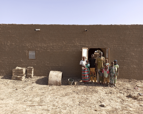 Famille debout devant l'entrée d'une maison en briques de terre, avec des briques empilées sur le côté