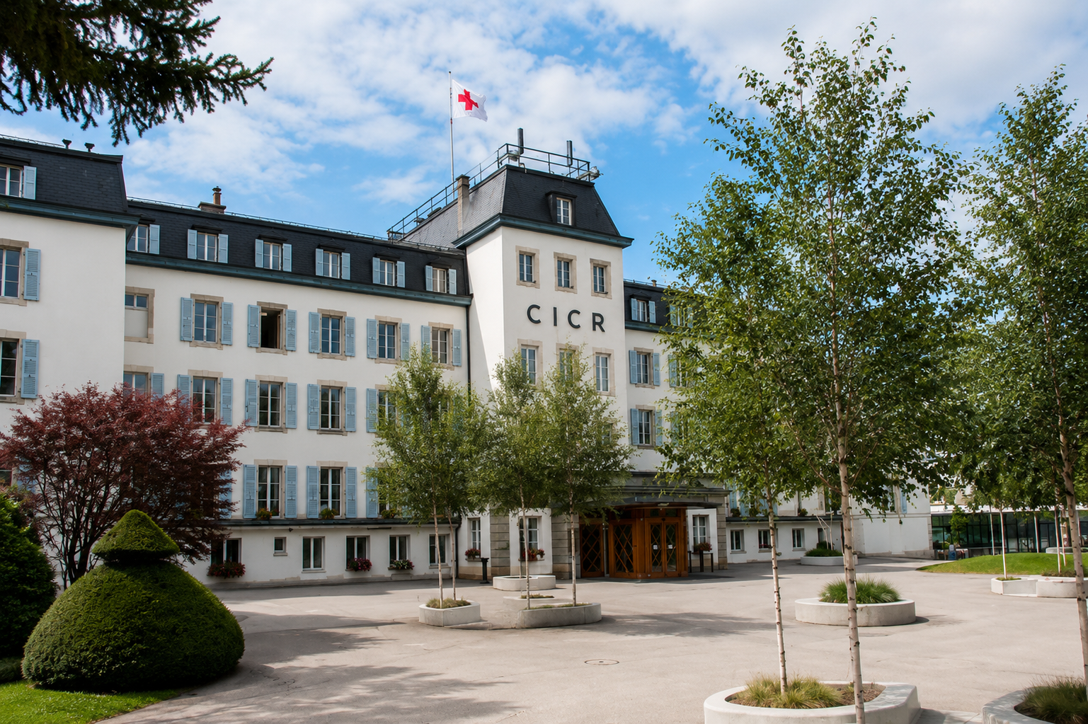 Bâtiment blanc à volets bleus surmonté d'un drapeau à croix rouge, avec l'inscription CICR sur la façade et des bouleaux devant