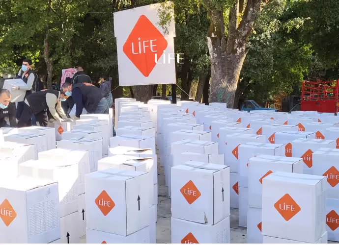 Bénévoles de LIFE portant des masques et alignant de nombreux cartons blancs à logo LIFE sous les arbres