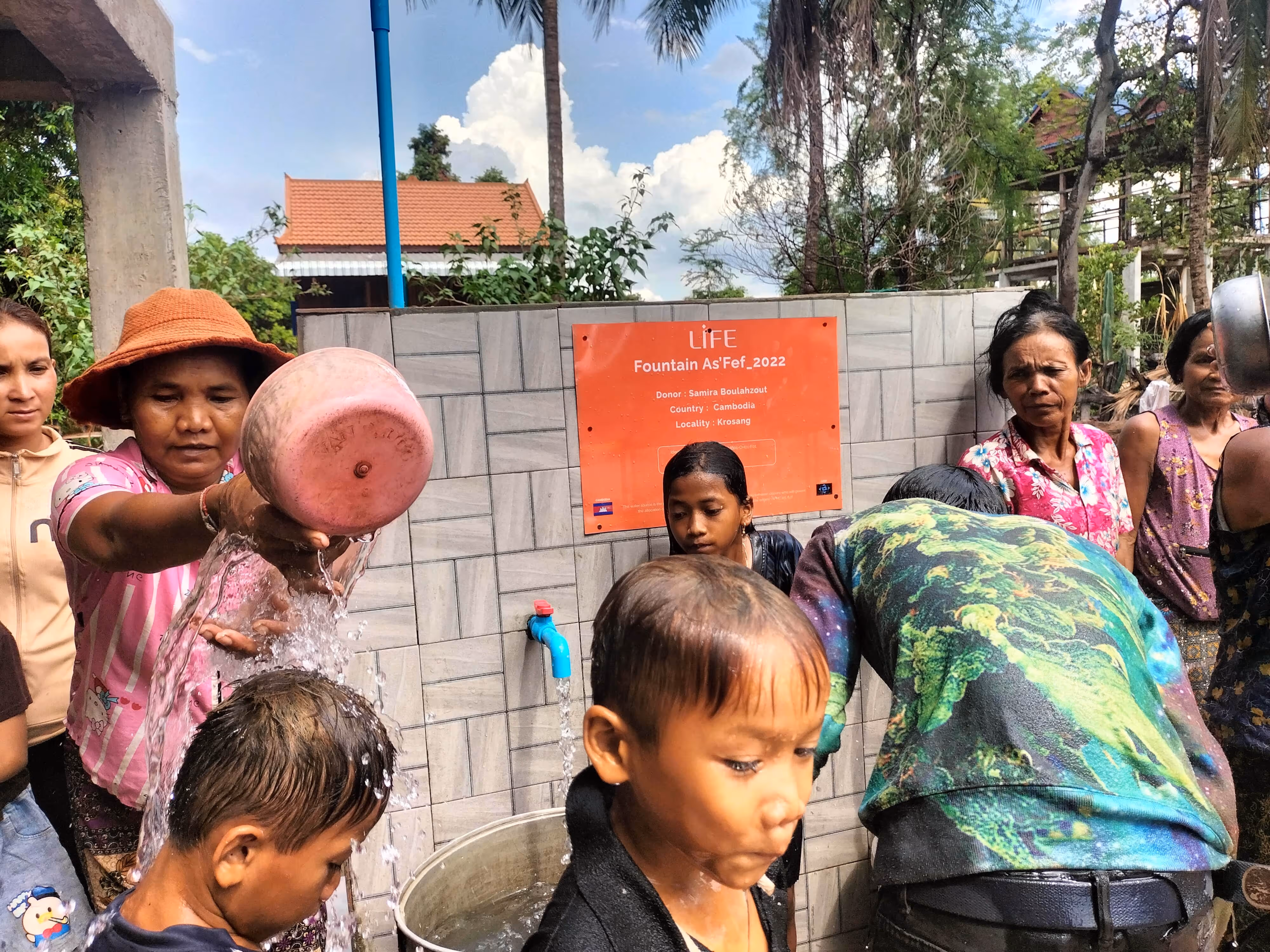 Des habitants du Cambodge s'aspergent et se rafraîchissent à une fontaine carrelée portant une plaque LIFE, à Krosang