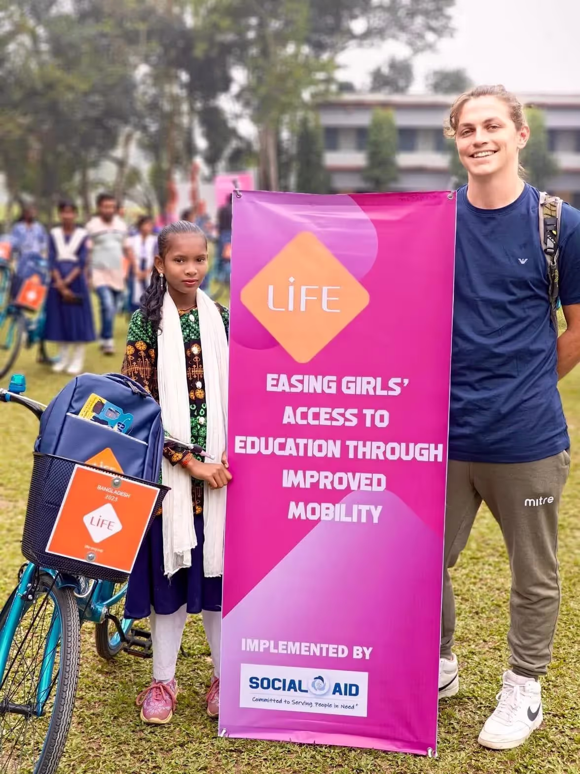 Jeune fille avec son vélo et un jeune homme posant près d'une bannière LIFE sur l'accès des filles à l'éducation