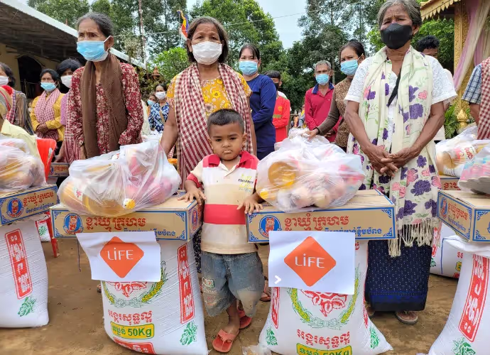 Distribution de sacs de riz et de colis alimentaires LIFE à des villageois masqués, avec un jeune enfant au premier plan