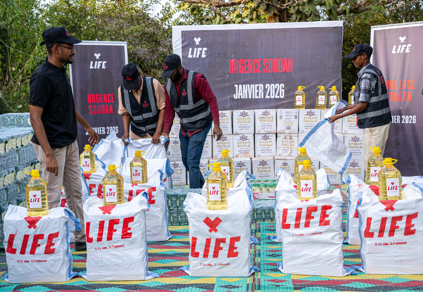 Quatre membres de LIFE préparent des sacs LIFE et des bidons d'huile devant des bannières « Urgence Soudan, janvier 2026 »
