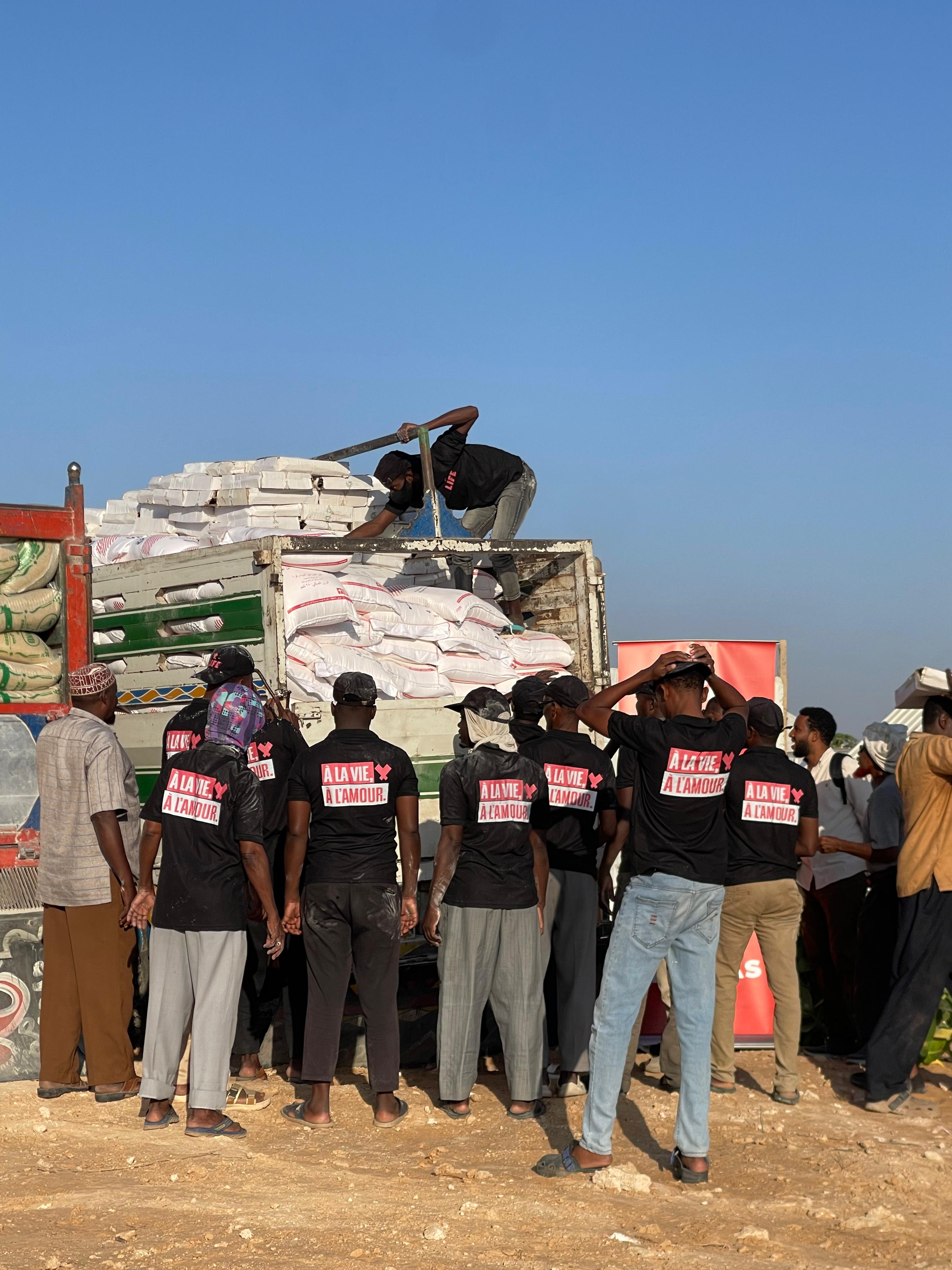 Des volontaires en t-shirt noir « À la vie à l'amour » déchargent des sacs d'un camion de distribution, entourés d'une foule
