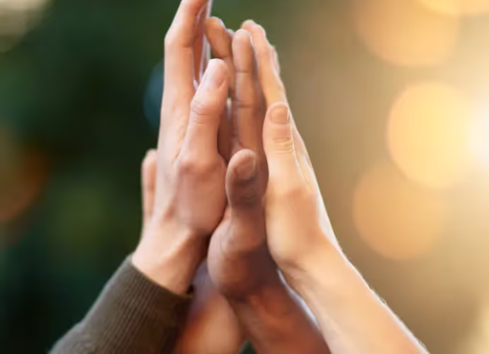 Gros plan de plusieurs mains levées qui se touchent, paume contre paume, sur fond flou vert et lumières dorées