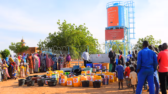 Foule de villageois et bidons orange alignés devant un château d'eau LIFE, lors d'une distribution d'eau dans un village