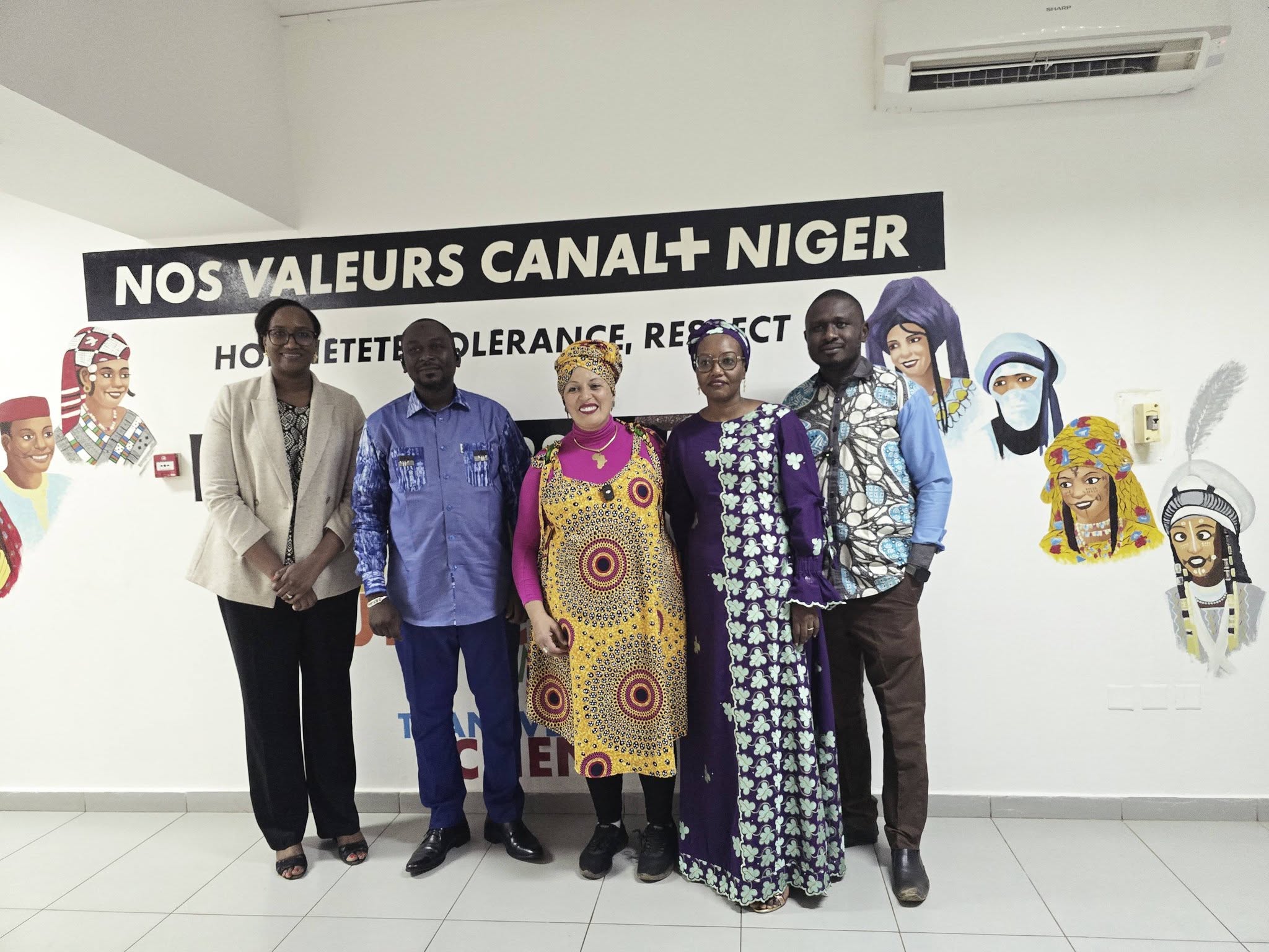 Cinq personnes posant côte à côte devant un mur peint portant l'inscription « Nos valeurs Canal+ Niger », avec des portraits illustrés