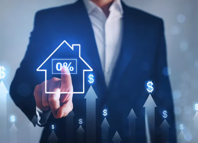 Main d'un homme en costume touchant une maison lumineuse marquée « 0% », entourée de flèches montantes et de symboles dollar
