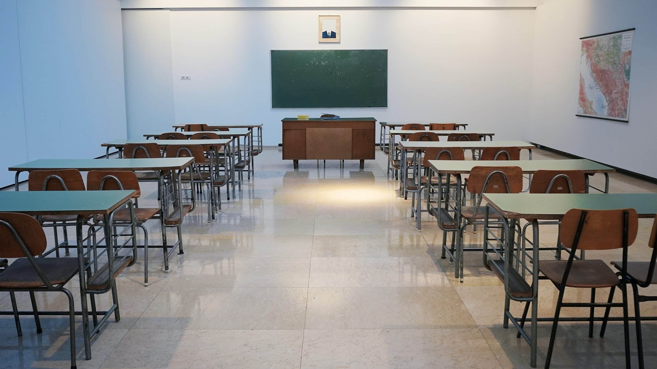 Salle de classe vide avec bureaux et chaises en bois alignés, tableau vert et carte accrochée au mur