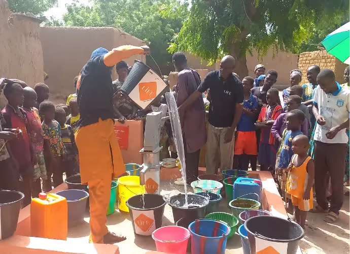 Des villageois et des enfants se pressent autour d'une pompe à eau LIFE où des seaux et bidons colorés sont remplis