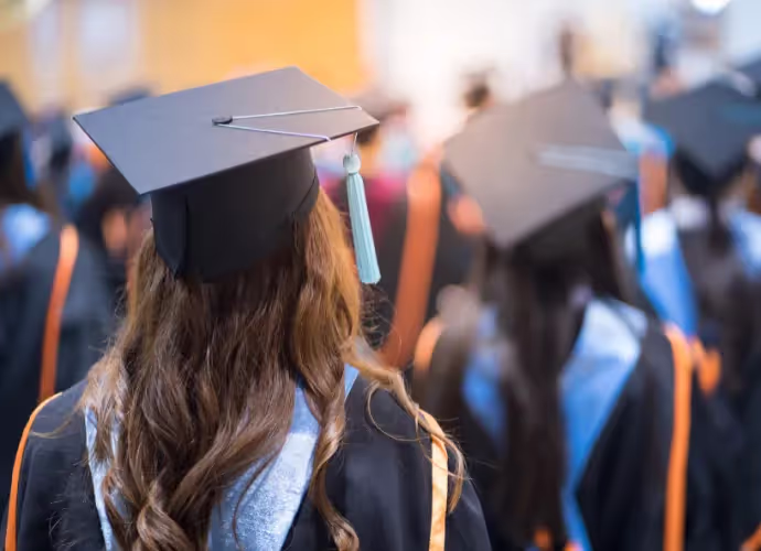 Étudiants diplômés vus de dos, portant toge et mortier, dont une jeune femme aux longs cheveux châtains