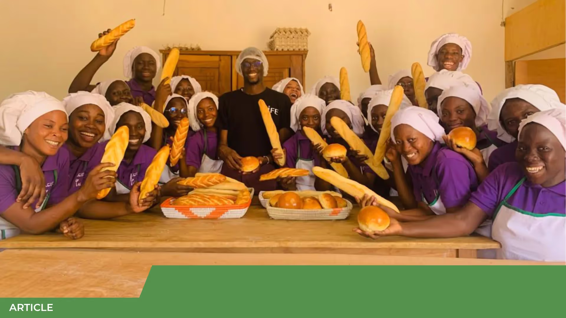 Groupe de jeunes femmes en tenue violette et charlottes blanches brandissant des baguettes et des pains dans une boulangerie