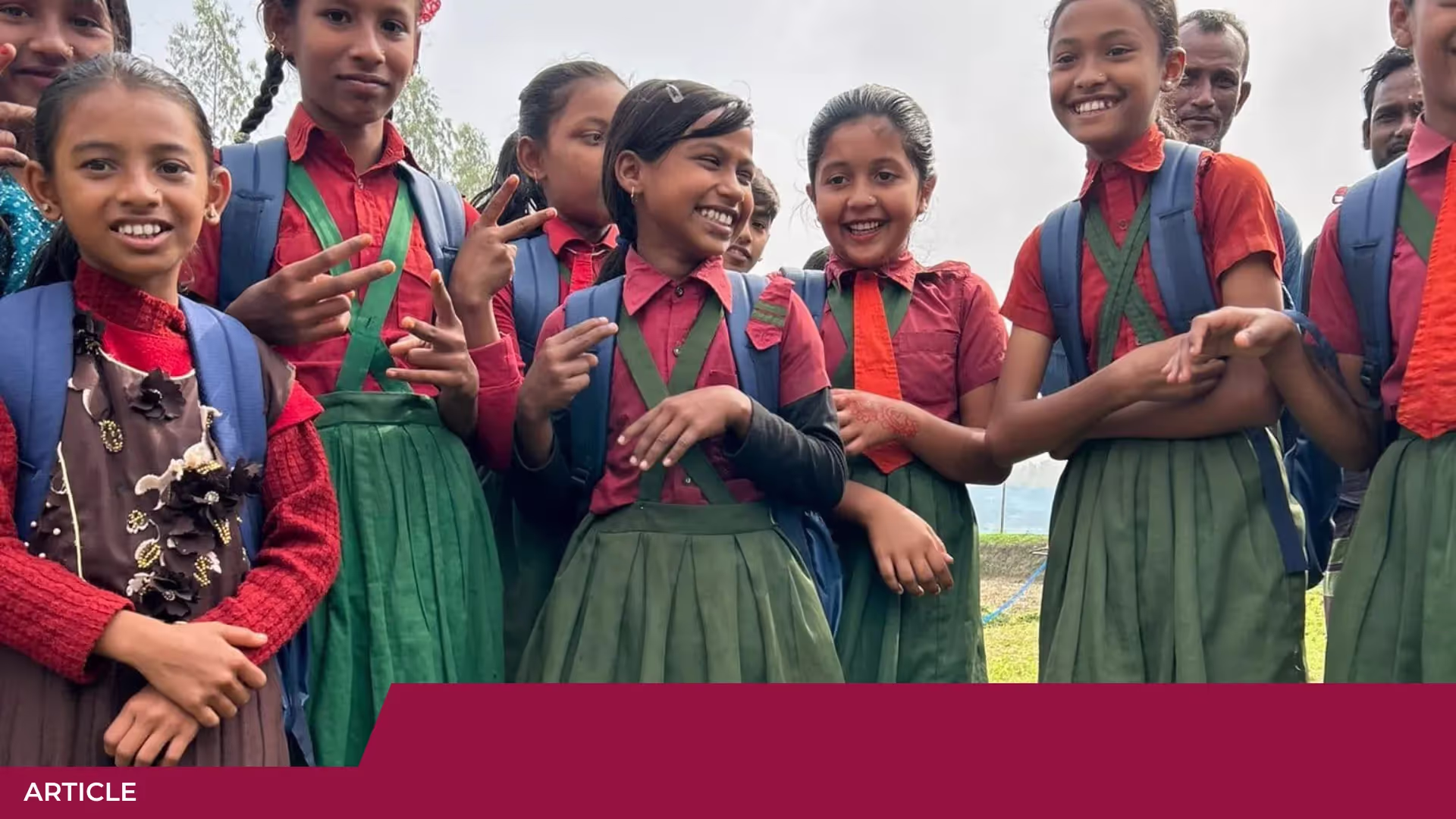 Groupe de jeunes écolières souriantes en uniforme rouge et vert, sac à dos bleu, certaines faisant le signe de la victoire