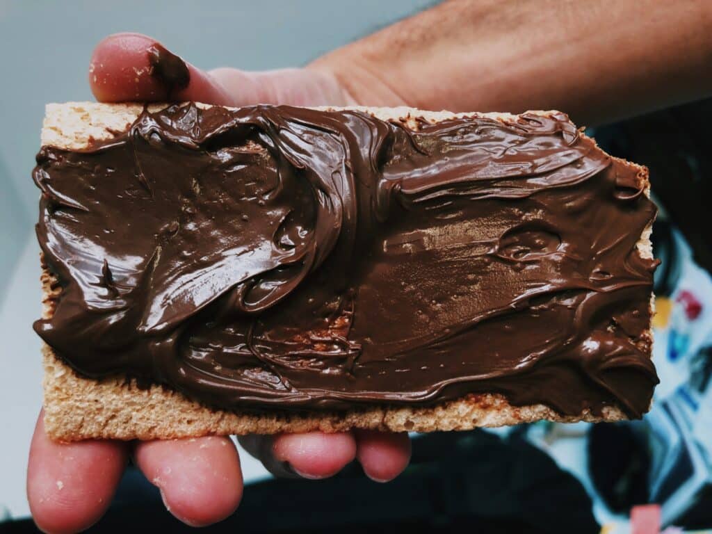 Main tenant une tranche de pain grillé ou biscuit épais largement tartinée de pâte à tartiner au chocolat