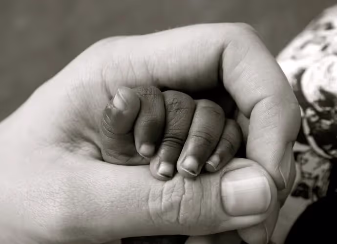 Photo en noir et blanc : la main d'un adulte referme doucement la petite main d'un bébé