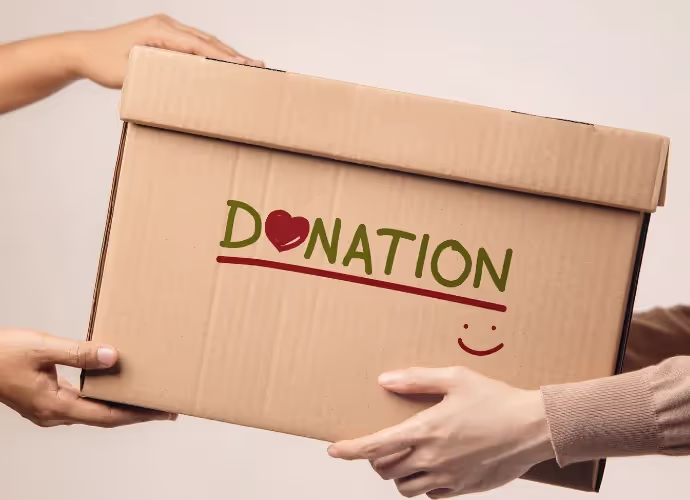 Des mains se passent un carton brun sur lequel est écrit « DONATION » avec un cœur rouge et un sourire dessiné