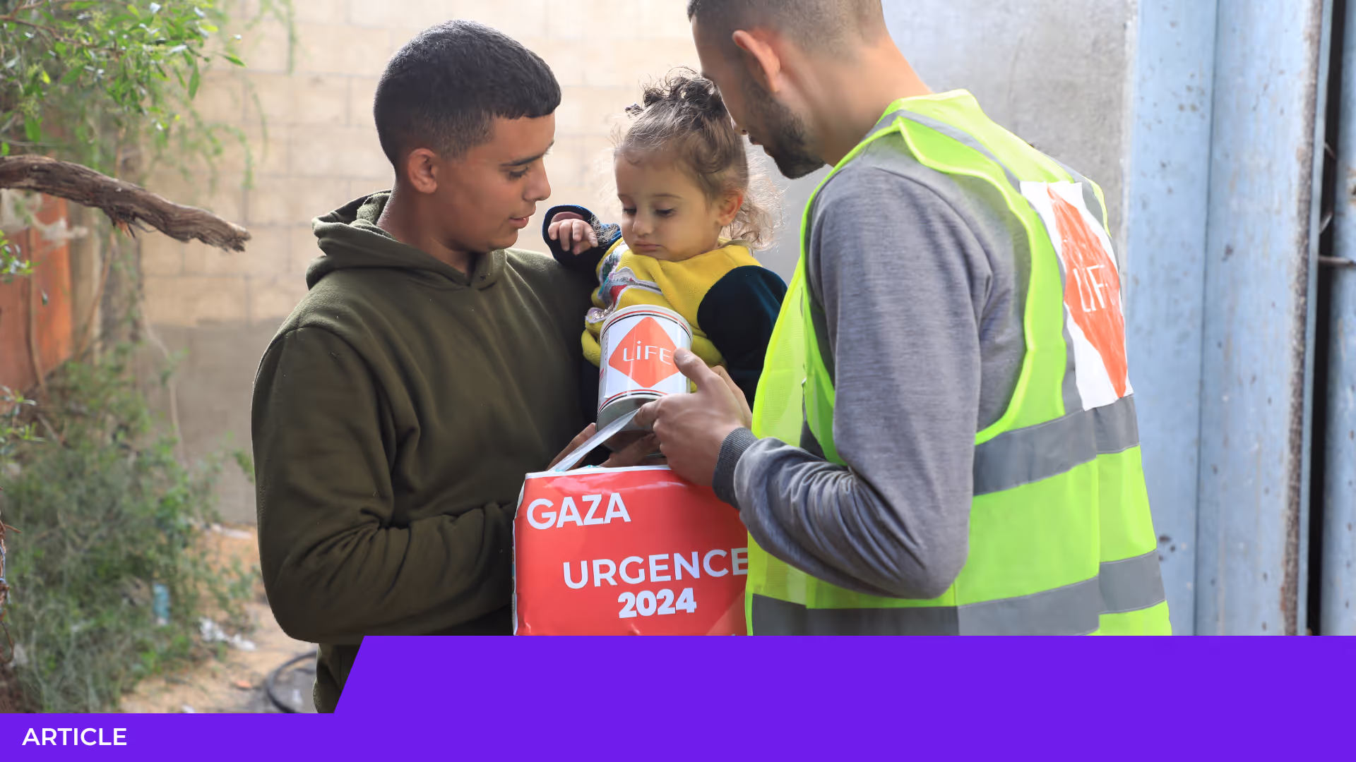 Deux hommes dont un en gilet jaune, et un jeune enfant, autour d'un colis LIFE « Gaza Urgence 2024 »