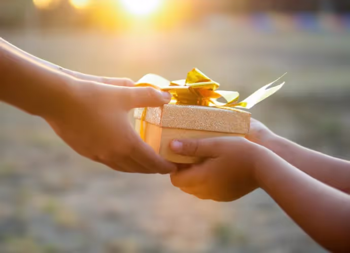 Deux mains échangent un petit coffret cadeau doré noué d'un ruban, dans la lumière du soleil couchant