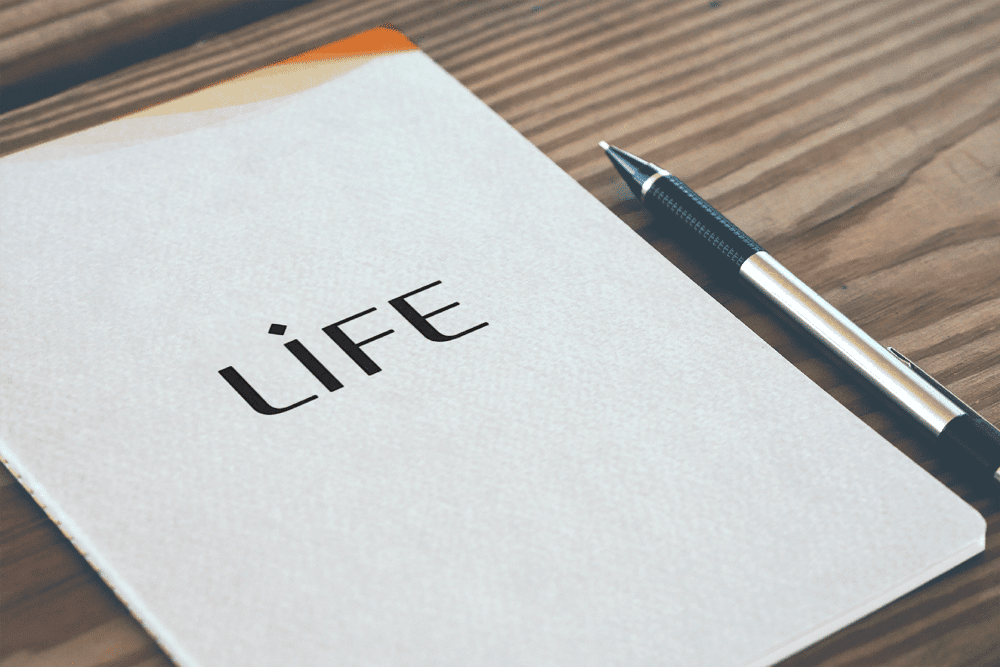 Cahier blanc portant le logo LIFE, posé sur une table en bois à côté d'un stylo