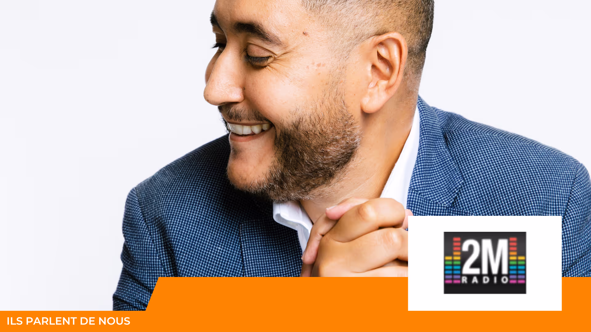 Portrait d'un homme barbu en veste bleue, souriant et regardant de côté, avec le logo de la radio 2M Radio en bas à droite