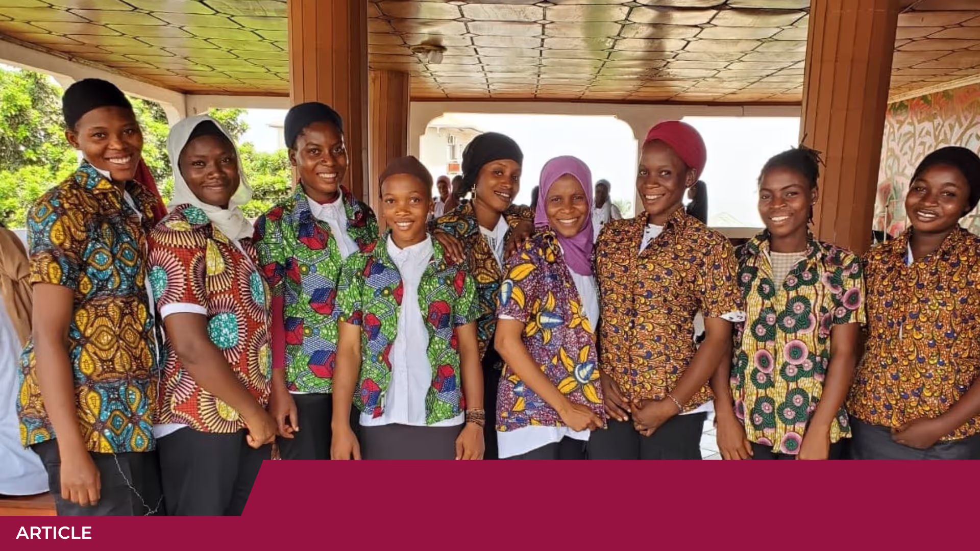 Huit jeunes femmes souriantes en chemises à motifs colorés posent côte à côte sous une galerie couverte