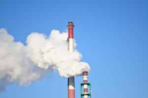 Deux hautes cheminées d'usine rouges et blanches rejetant un épais panache de fumée blanche dans un ciel bleu