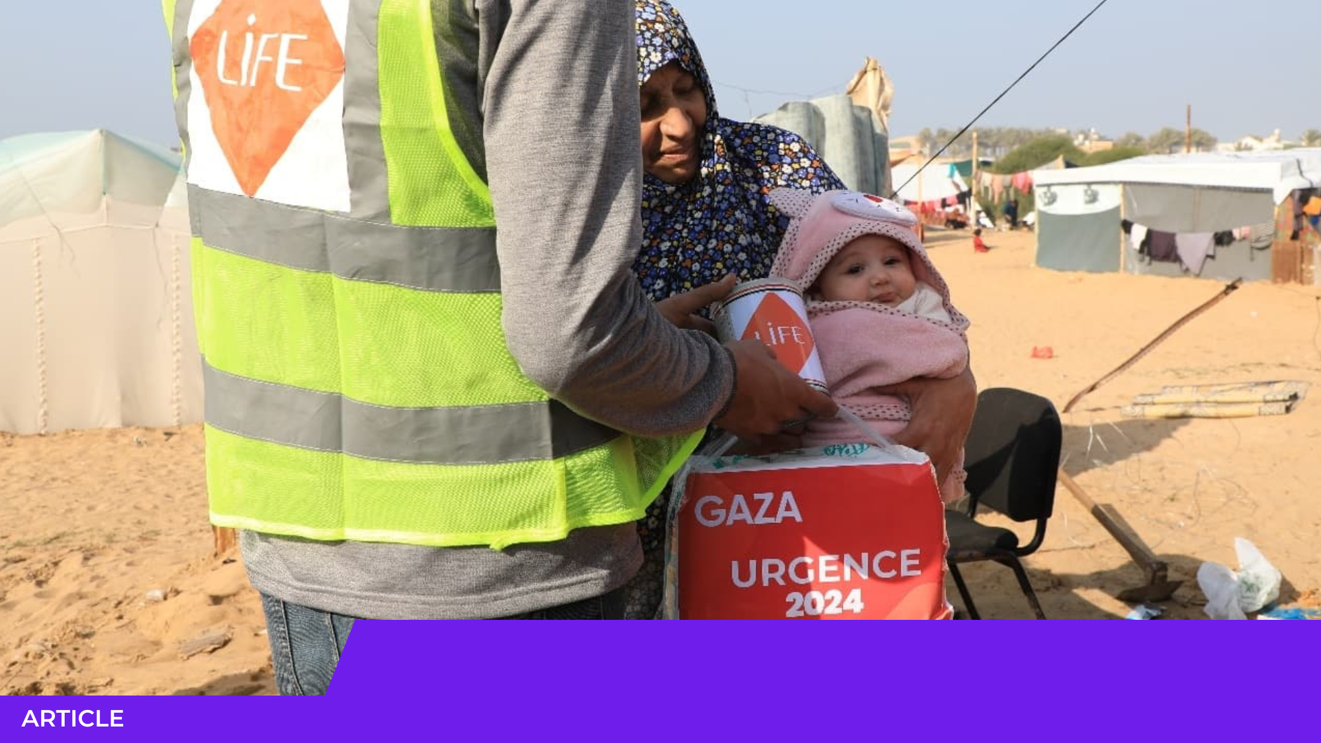 Un bénévole en gilet jaune LIFE remet un colis « Gaza Urgence 2024 » à une femme portant un bébé, dans un camp de tentes