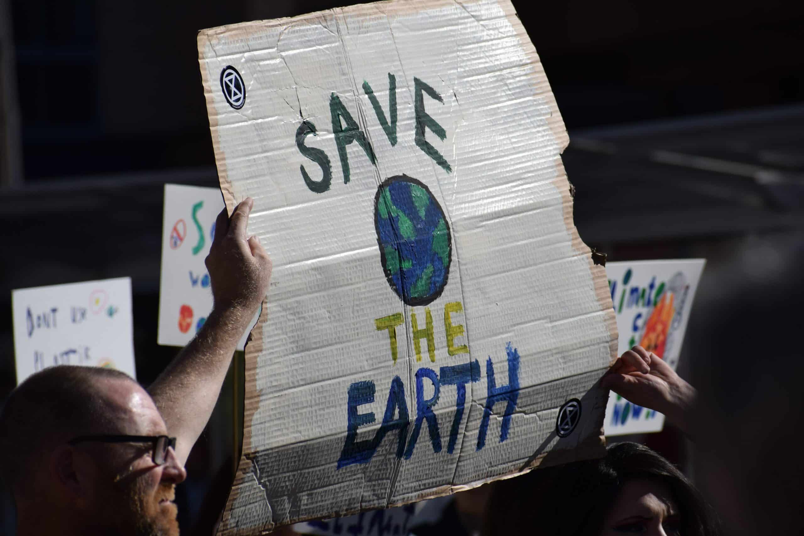 Manifestant brandissant une pancarte en carton peinte « Save the Earth » avec un globe, parmi d'autres pancartes