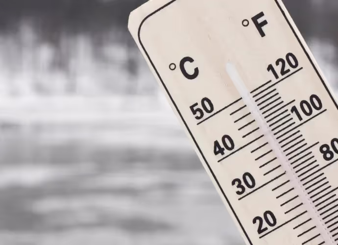 Thermomètre en bois gradué en degrés Celsius et Fahrenheit, devant un arrière-plan gris flou