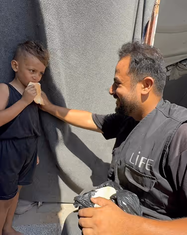 Geste solidaire à Gaza : un bénévole LIFE offre du pain à un enfant lors d’une distribution humanitaire. Aider gaza, soutien palestine.