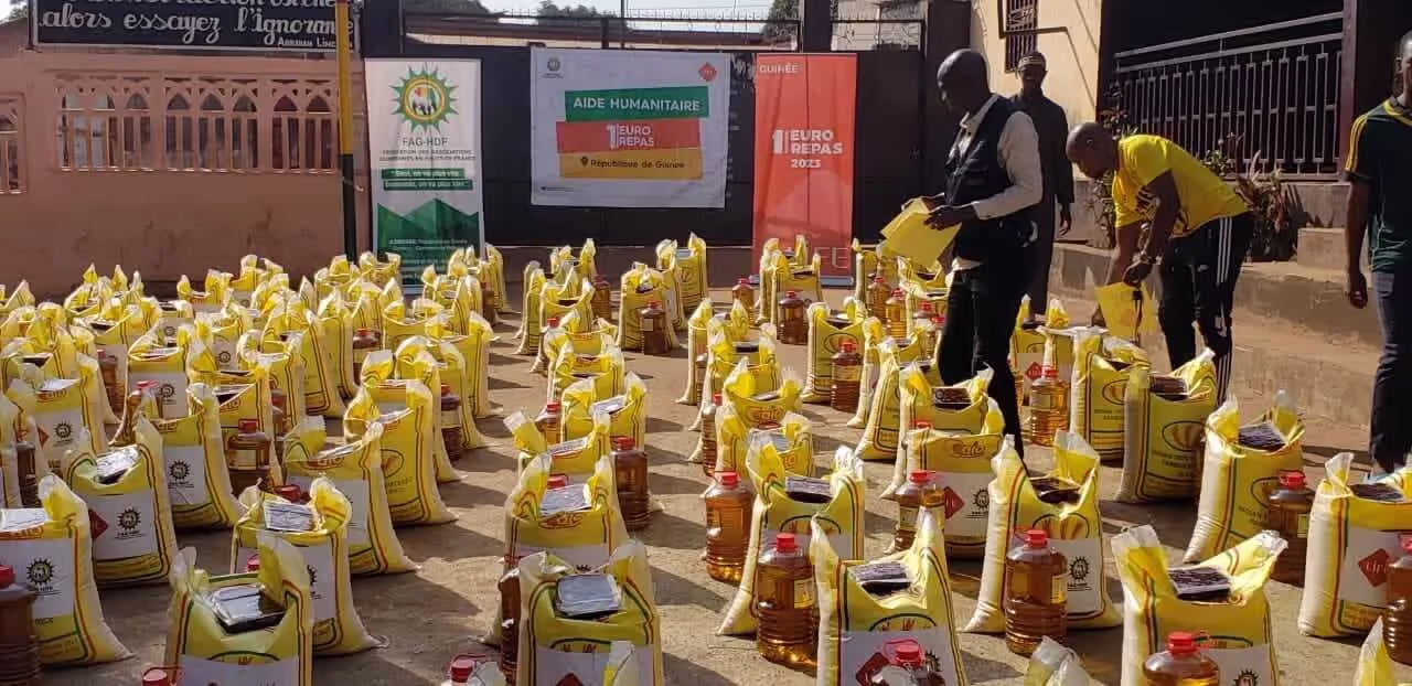 Des sacs de riz et des bouteilles d'huile alignés dans une cour lors d'une distribution d'aide humanitaire, avec des hommes en train de les préparer