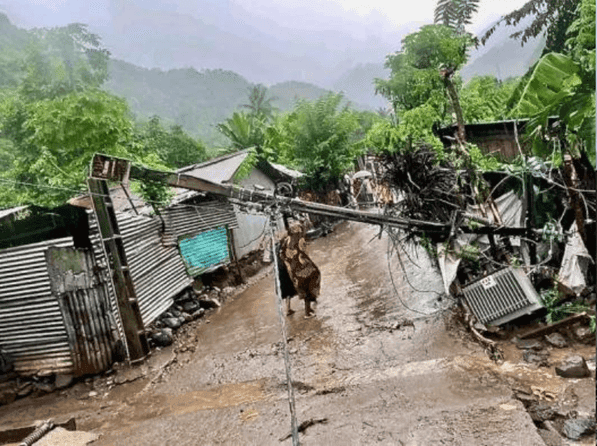 Rue boueuse d'un village de montagne après une catastrophe, poteau électrique tombé et maisons en tôle endommagées