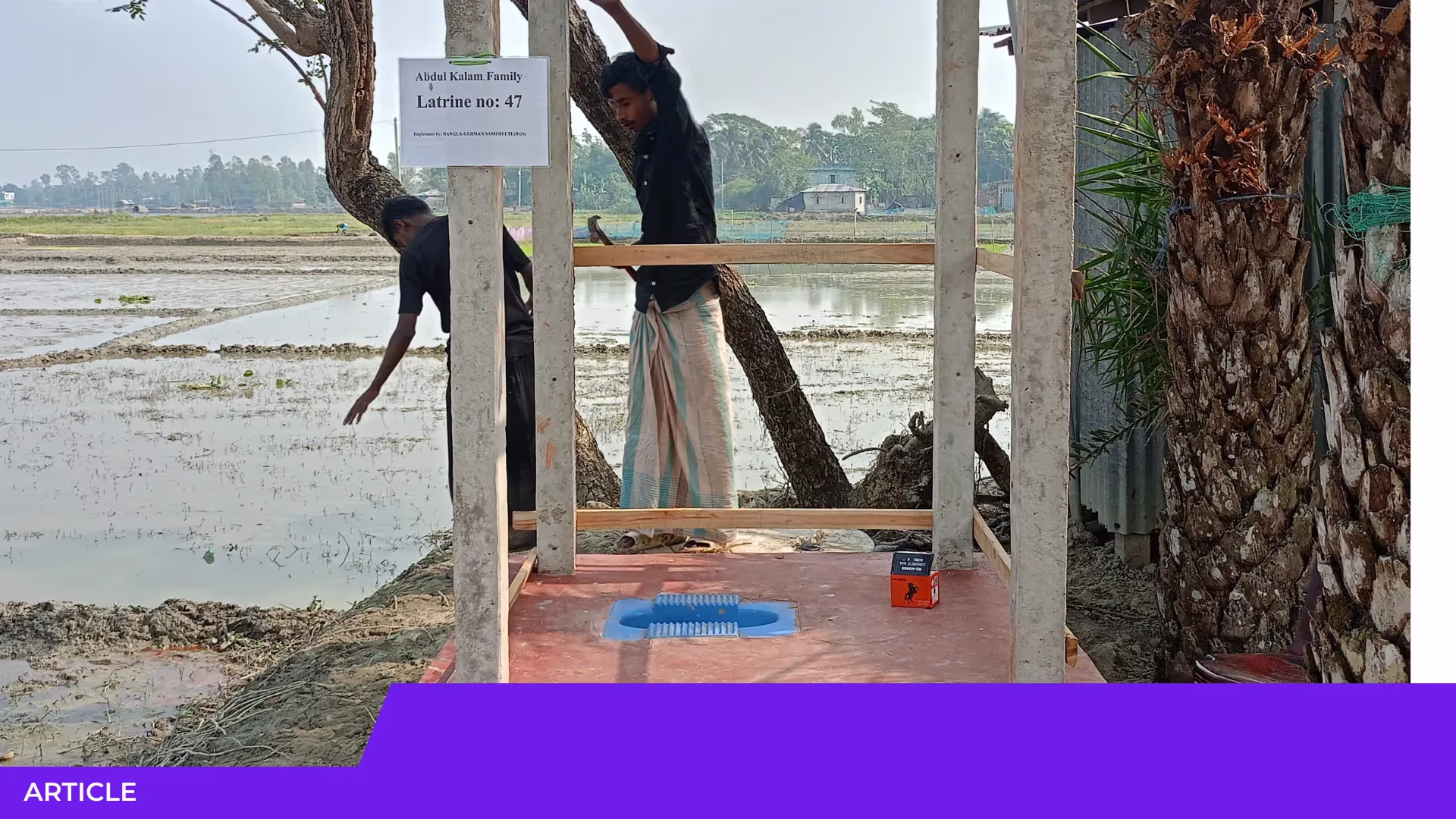 Deux hommes construisent une latrine en béton et bois au bord d'une rizière inondée ; un écriteau indique la latrine no 47