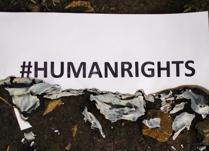 Feuille blanche portant le mot-dièse #HUMANRIGHTS, dont le bord est brûlé, posée sur de la terre sombre et des pierres